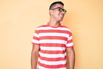 Young handsome latin man wearing casual clothes and glasses looking away to side with smile on face, natural expression. laughing confident.