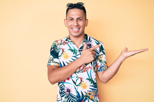 Young handsome latin man wearing summer clothes amazed and smiling to the camera while presenting with hand and pointing with finger.