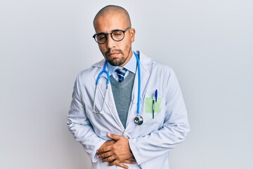 Hispanic adult man wearing doctor uniform and stethoscope with hand on stomach because indigestion, painful illness feeling unwell. ache concept.