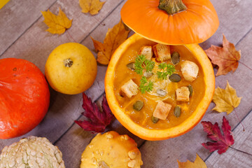 Pumpkin cream soup. Vegetarian autumn pumpkin carrot soup in a hollow pumpkin with cream, pumpkin seeds, parsley, and croutons. Autumn thanksgiving colorful decoration with wood, leaves and pumpkins.