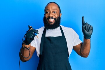 Young african american man tattoo artist wearing professional uniform and gloves holding tattooer...