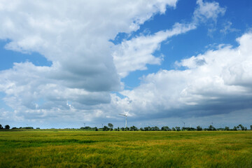 Panorama-foto von ostfriesischer Landschaft im Sommer mit Getreidefeld und Windrädern und großen weißen wolken vor blauem himmel - Stockfoto