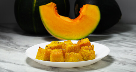 Baked pumpkin in a white plate. Side view. Pumpkin cooked in the oven. Cut pieces of pumpkin.A traditional autumn dish of baked pumpkin. Close-up.