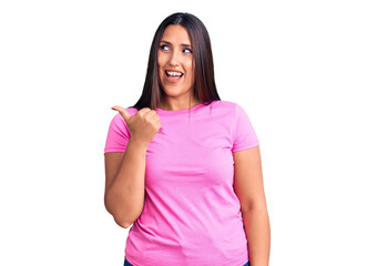 Fototapeta premium Young beautiful brunette woman wearing casual t-shirt smiling with happy face looking and pointing to the side with thumb up.