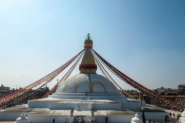 A panoramic view at the Boudhanath Temple in Kathmandu, Nepal. Golden face of Buddha shines bright. Many prayer flags surrounding the top. Bright blue sky. Wisdom eyes.