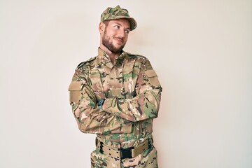 Young caucasian man wearing camouflage army uniform looking to the side with arms crossed convinced and confident