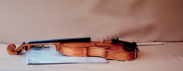 Elegant brown wooden violin with bow and light blue folder for music sheets lying on white table near wall in light room close view. Traditional instrument. © lusyaya