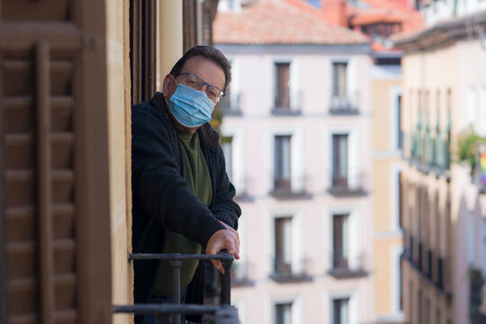 mature man in balcony home lockdown during covid19 outbreak - senior male on his 70s in face mask worried and tired looking to the street thoughtful and depressed in quarantine