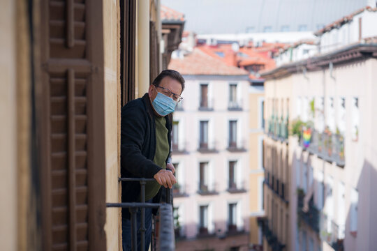 mature man in balcony home lockdown during covid19 outbreak - senior male on his 70s in face mask worried and tired looking to the street thoughtful and depressed in quarantine