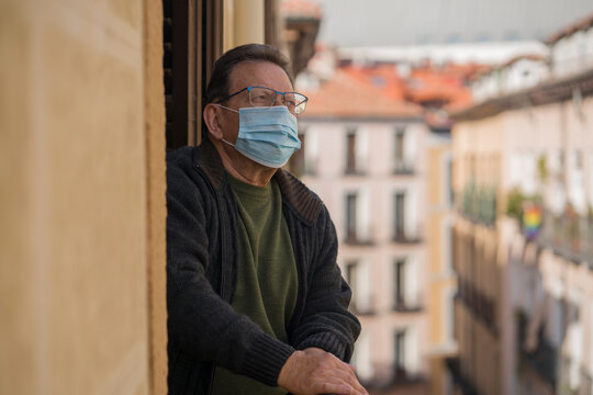 mature man in balcony home lockdown during covid19 outbreak - senior male on his 70s in face mask worried and tired looking to the street thoughtful and depressed in quarantine