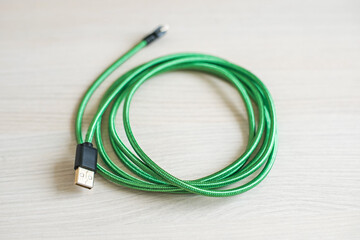 Fototapeta premium Contemporary coiled usb cable with green covering case lying on textured wooden table at bright light extreme close view. Electric connection equipment.