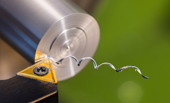 Beautiful spiral metal swarf. Close-up of turning on green background. Detail of lathe tool bit with yellow triangle carbide insert when working dural cylindric workpiece. Twisted alu chip. Machining.