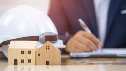 Focus at miniature house with blurred background of architect hand planing his project works on marble table in office room