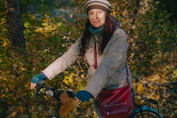 Fototapeta na wymiar Pretty brunette leans on bicycle in autumn park