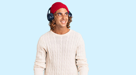 Young hispanic man listening to music using headphones smiling looking to the side and staring away thinking.