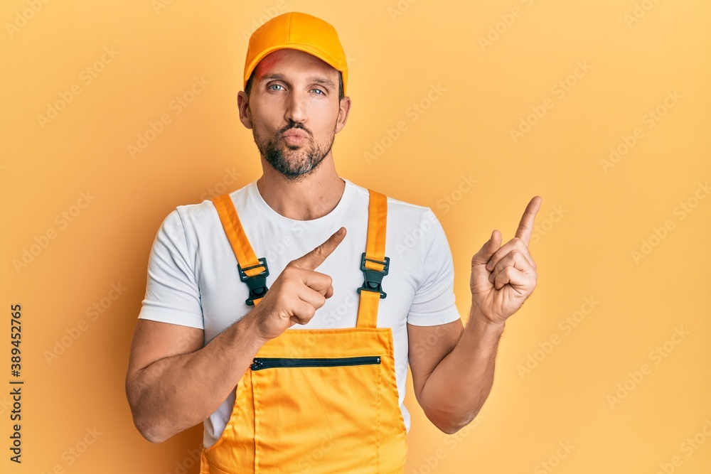 Sticker Young handsome man wearing handyman uniform pointing to the side looking at the camera blowing a kiss being lovely and sexy. love expression.