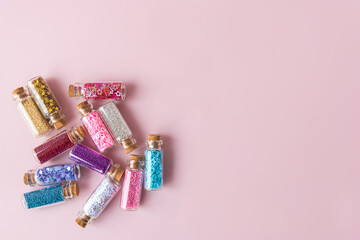 Numerous of glass bottles with different bright color shiny glitters closed with corks on pink background flat lay with space for text. Festive decoration.