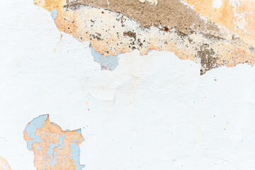 Grunge texture of ancient building wall covered with white chipped stucco at bright sunlight on city street close view. Traditional architectural style.