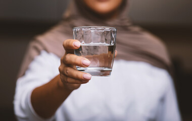 Unrecognizable Muslim Woman Offering Glass Of Water To Camera Indoors
