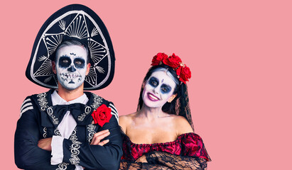 Fototapeta premium Young couple wearing mexican day of the dead costume over background happy face smiling with crossed arms looking at the camera. positive person.
