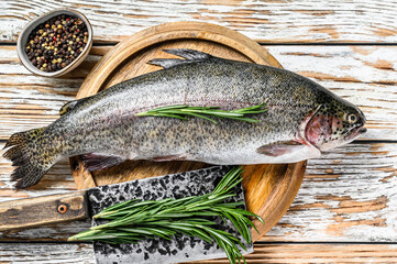 Rainbow trout on an wood board, with rosemary and cleaver. White wooden background. Top view - obrazy, fototapety, plakaty