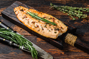Baked trout fillet on a cutting board. Dark  wooden background. Top view - obrazy, fototapety, plakaty
