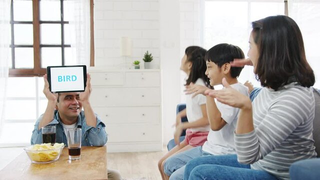 Happy cheerful Asia family having fun using digital tablet play game hobby at sofa couch in living room at home. Spending time together, Social distancing, Quarantine for corona virus prevention.