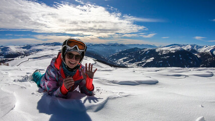 Fototapeta na wymiar A woman lying in powder snow any enjoying the sun on top of Katschberg in Austria. She is happy and joyful. Panoramic view on the surrounding mountains. Winter wonderland, Clear and sunny winter day