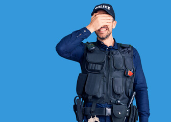 Young handsome man wearing police uniform smiling and laughing with hand on face covering eyes for...