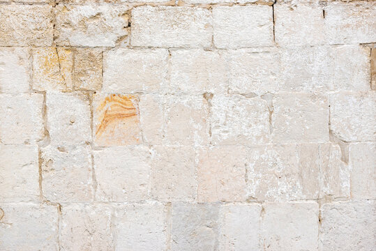White wall of ancient building made with old limestone bricks with orange stroke at bright sunlight on city street close view. Traditional architectural style.