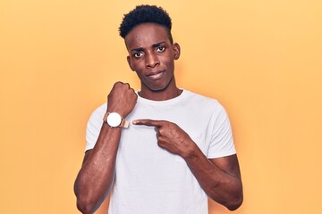 Young african american man wearing casual clothes in hurry pointing to watch time, impatience,...