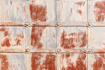 Wonderful old metal door surface with decorative grid and strokes of chipped paint at bright sunlight on city street extreme closeup. Traditional architecture.