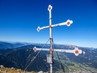 A cross on top of Kaiserau Kreuzkogel, Austrian Alps. The cross has transverse arms. Behind it there is a panoramic view on the whole region. Clear and bright day. Achievement