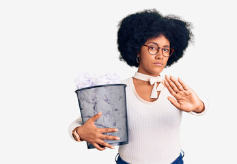 Young african american girl holding paper bin full of crumpled papers with open hand doing stop sign with serious and confident expression, defense gesture