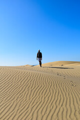 Lonely traveler walking through desert sand dunes with backpack.