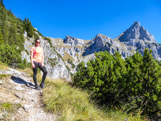 Naklejka na ściany i meble A woman hiking in a massive, stony mountains in Kaiserau Kreuzkogel region, Austrian Alps. She is enjoying the Alpine landscape. Many sharp peaks surrounding her. Sunny summer day