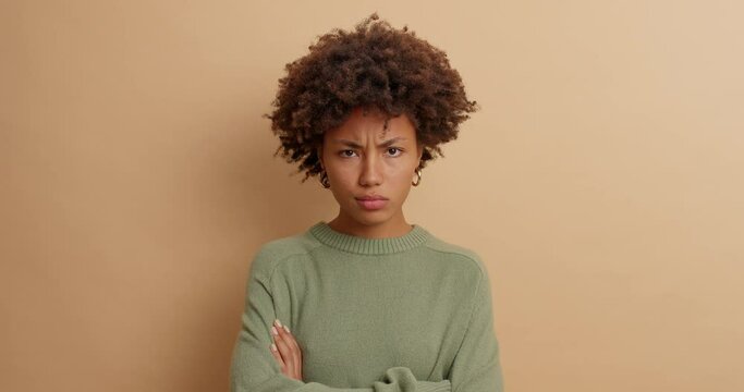 Irritated angry wife listens to husbands explanations crosses arms over body and looks with annoyed expression at camera dressed in casual jumper isolated over brown background. Negative feelings