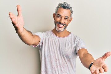 Middle age grey-haired man wearing casual clothes looking at the camera smiling with open arms for hug. cheerful expression embracing happiness.