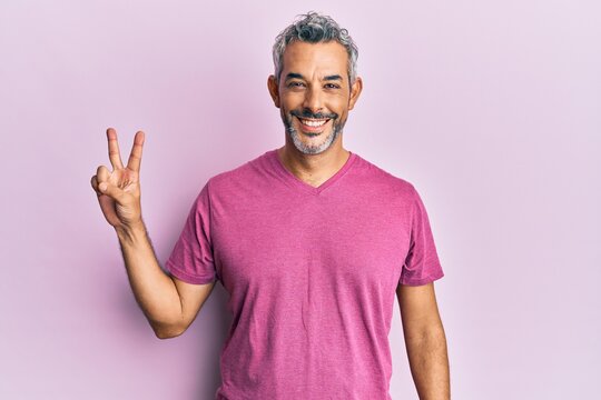 Middle age grey-haired man wearing casual clothes smiling with happy face winking at the camera doing victory sign. number two.