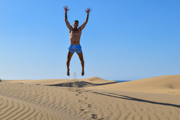 Fototapeta na wymiar Man on vacation, running and jumping in the desert sand dunes.