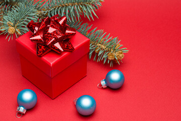Red Christmas gift box with colored ribbon and Christmas balls on a red background.