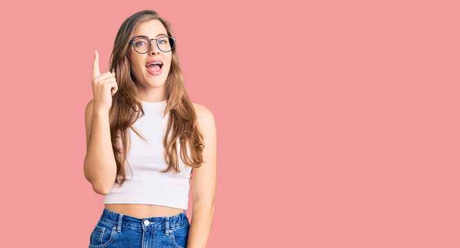 Beautiful caucasian young woman wearing casual clothes and glasses pointing finger up with successful idea. exited and happy. number one.