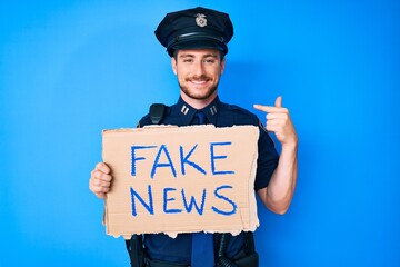 Young caucasian man wearing police uniform holding fake news banner pointing finger to one self...