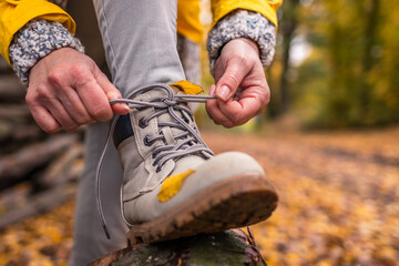 Woman tying shoelace on her hiking boot. Tourist is getting ready for autumn hike in forest - obrazy, fototapety, plakaty
