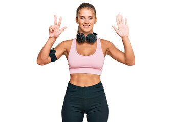 Young blonde woman wearing gym clothes and using headphones showing and pointing up with fingers number eight while smiling confident and happy.