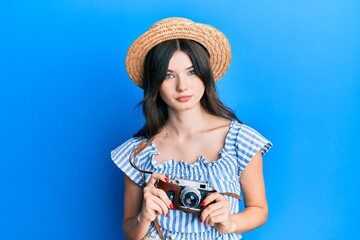 Young beautiful caucasian girl holding vintage camera relaxed with serious expression on face. simple and natural looking at the camera.