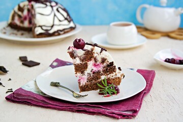 Dessert, sliced homemade cake with chocolate biscuit, cherry and cream of sour cream and whipped cream on a white plate