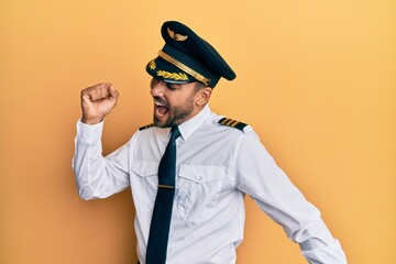 Handsome hispanic man wearing airplane pilot uniform dancing happy and cheerful, smiling moving casual and confident listening to music