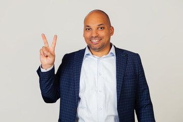 Portrait of a successful young African American businessman guy, showing with fingers to number two, smiling, confident and happy. The man shows two fingers. Number 2. Standing on a gray background.