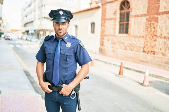 young handsome hispanic policeman wearing police uniform. Standing with serious expression at town street.